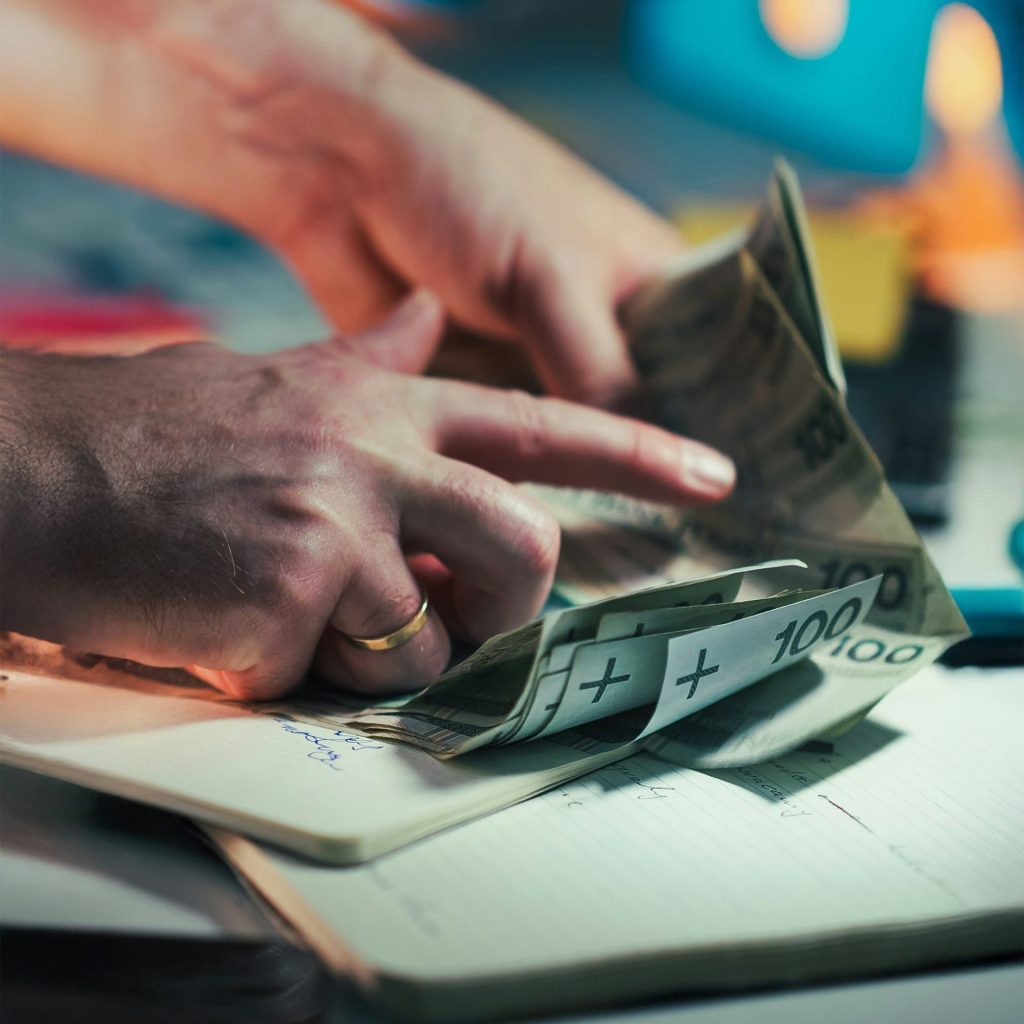 Hands counting polish banknotes on a notebook.